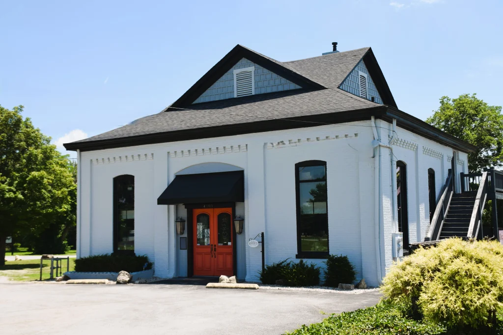 White-painted historic brick building with red doors and black awning in Buckner KY