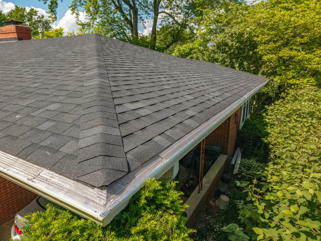 Newly installed gutter guards on a shingle roof of a Kentucky home surrounded by trees.