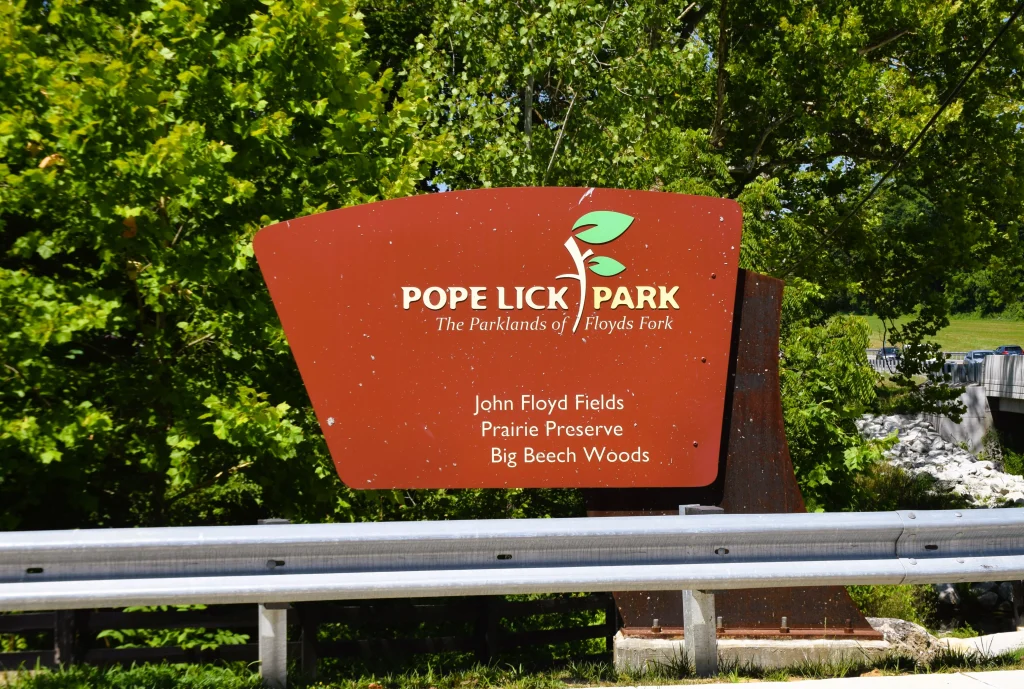 Entrance sign for Pope Lick Park in Fisherville, Kentucky surrounded by green trees