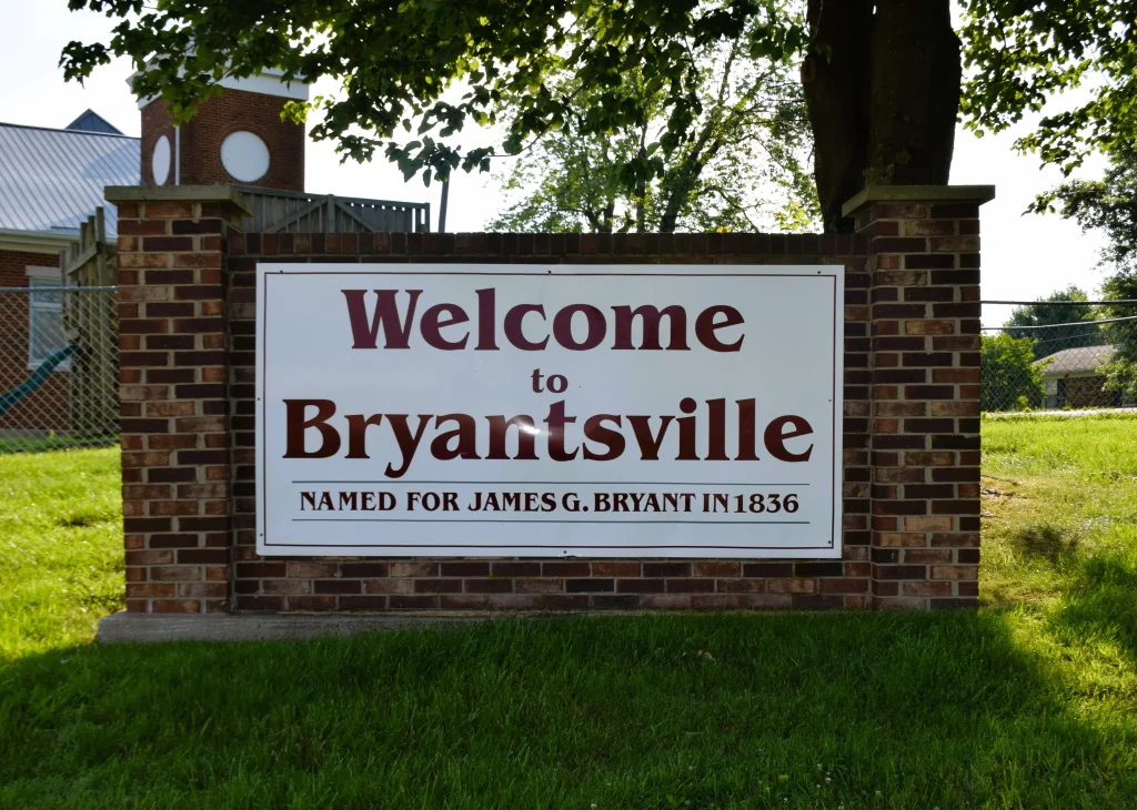 Welcome to Bryantsville sign with brick base and trees in the background