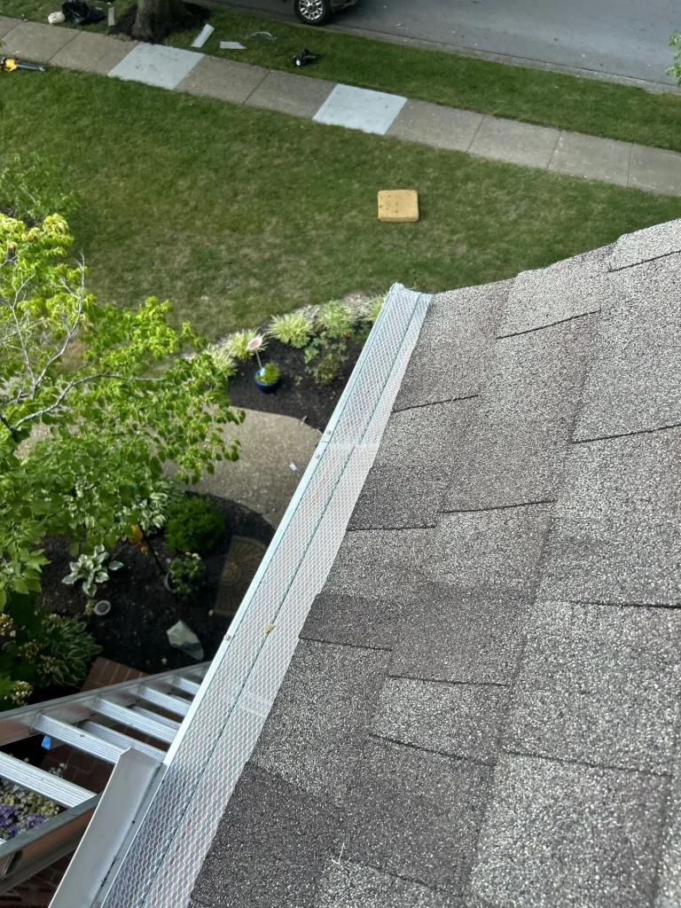 AIC Roofing Louisville Gutter Guard Installation New aluminum mesh gutter guard installed by AIC Roofing & Construction along the eave of a Louisville home, with ladder and yard below.