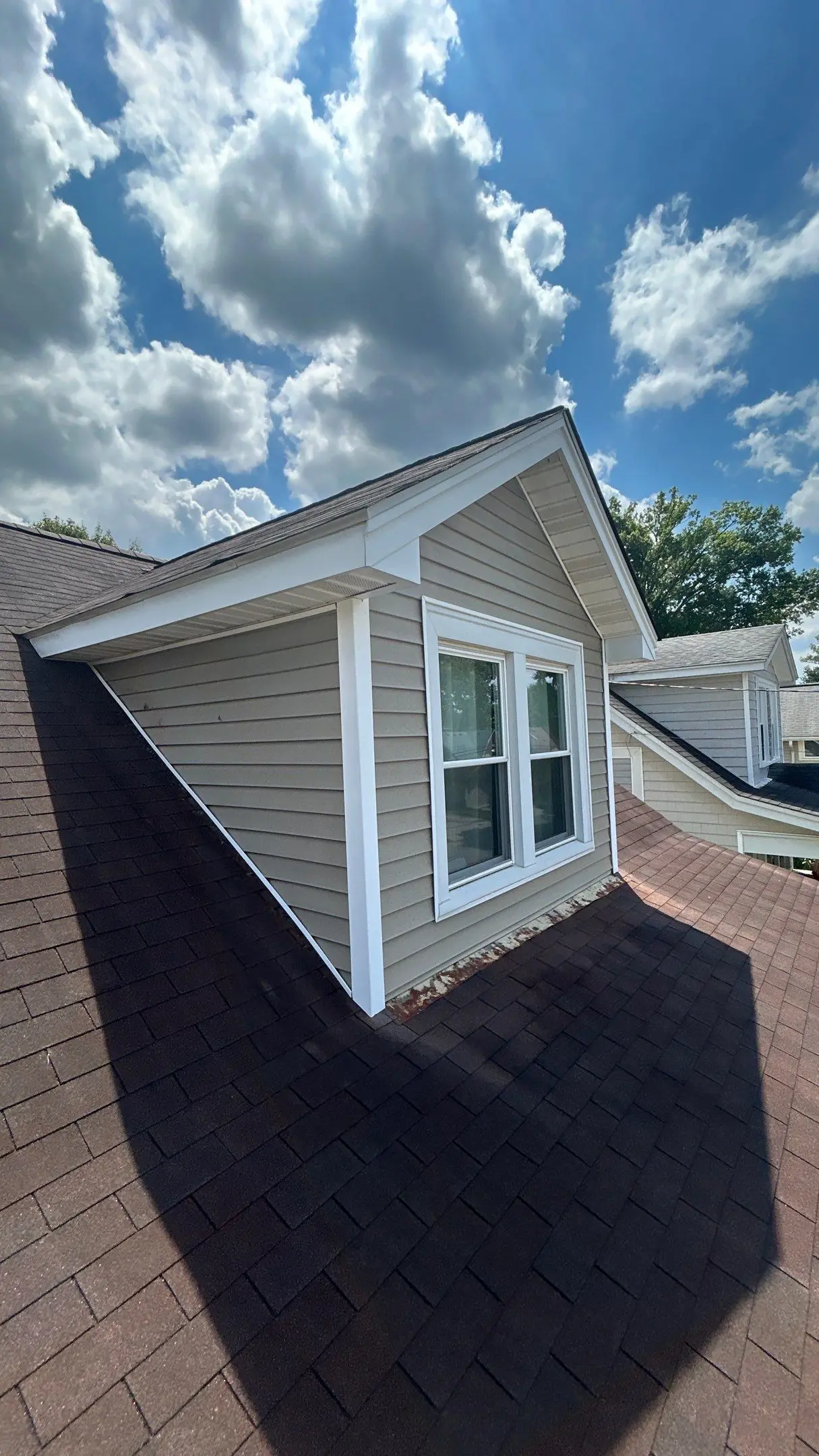 Dormer Roof-to-Wall Flashing on Louisville Home Dormer with tan siding and white trim on brown asphalt shingles; roof-to-wall flashing at the base shows rust on a Louisville home.