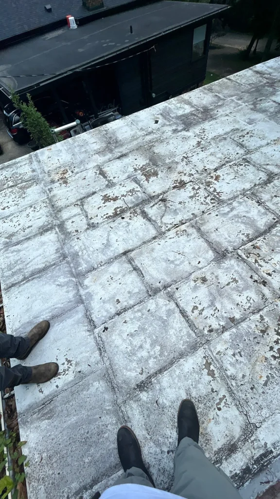 Flat Roof Coating Wear and Seam Cracks in Louisville Flat roof with worn white coating, peeling patches, and cracked seams on a Louisville home, with two inspectors’ boots visible.
