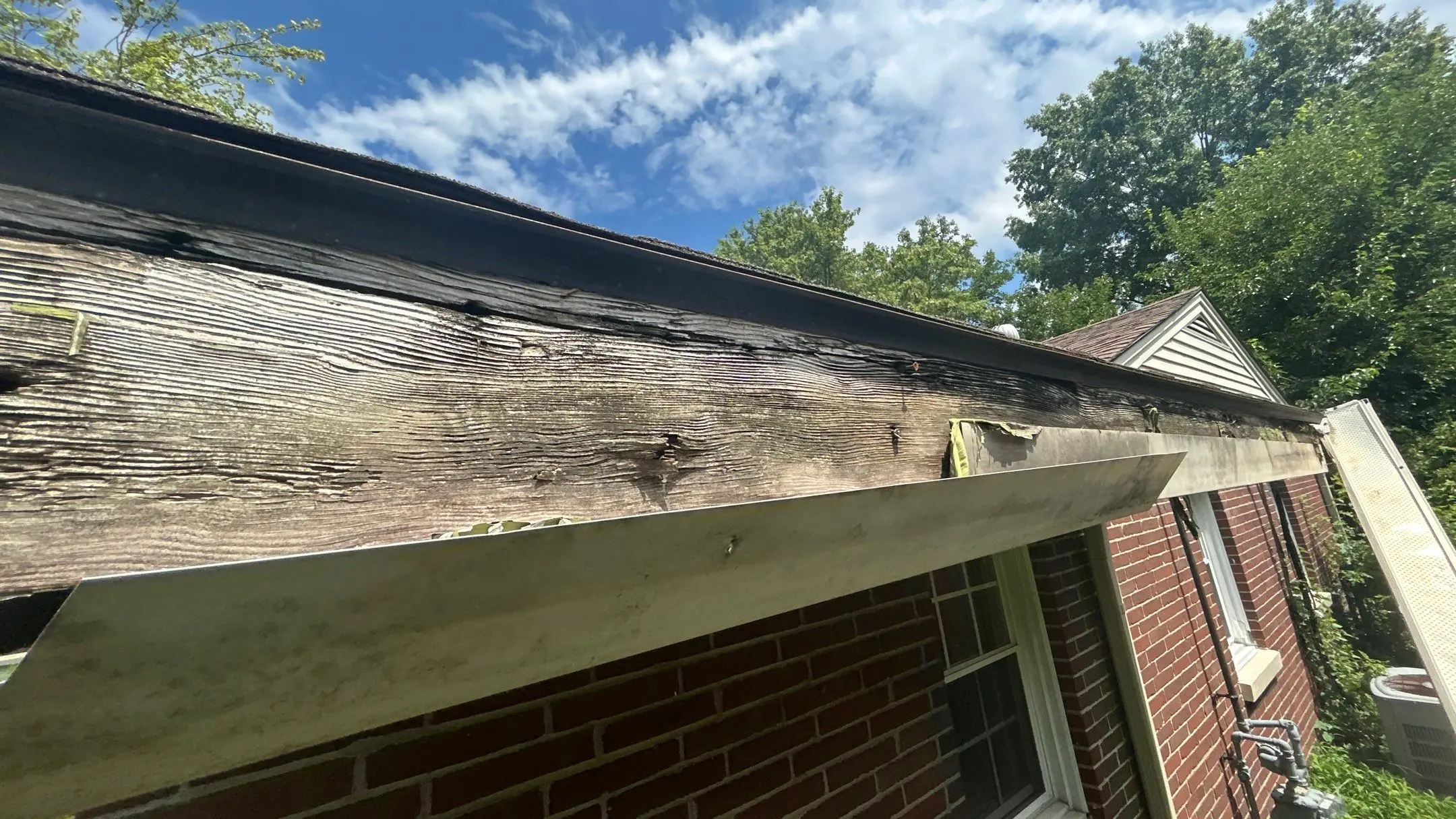 Louisville KY Fascia Damage – Before Gutter Replacement | AIC Roofing & Construction Close-up of rotted, weathered fascia board with detached fascia wrap at the roof eave of a Louisville, KY brick home, documented by AIC Roofing & Construction.