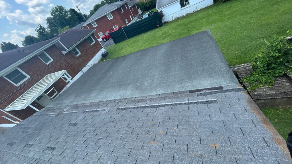 Louisville KY Roof Damage Inspection | AIC Roofing & Construction Overhead view of a Louisville, KY roof showing wind-damaged asphalt shingles with granule loss and missing tabs next to a low-slope section.
