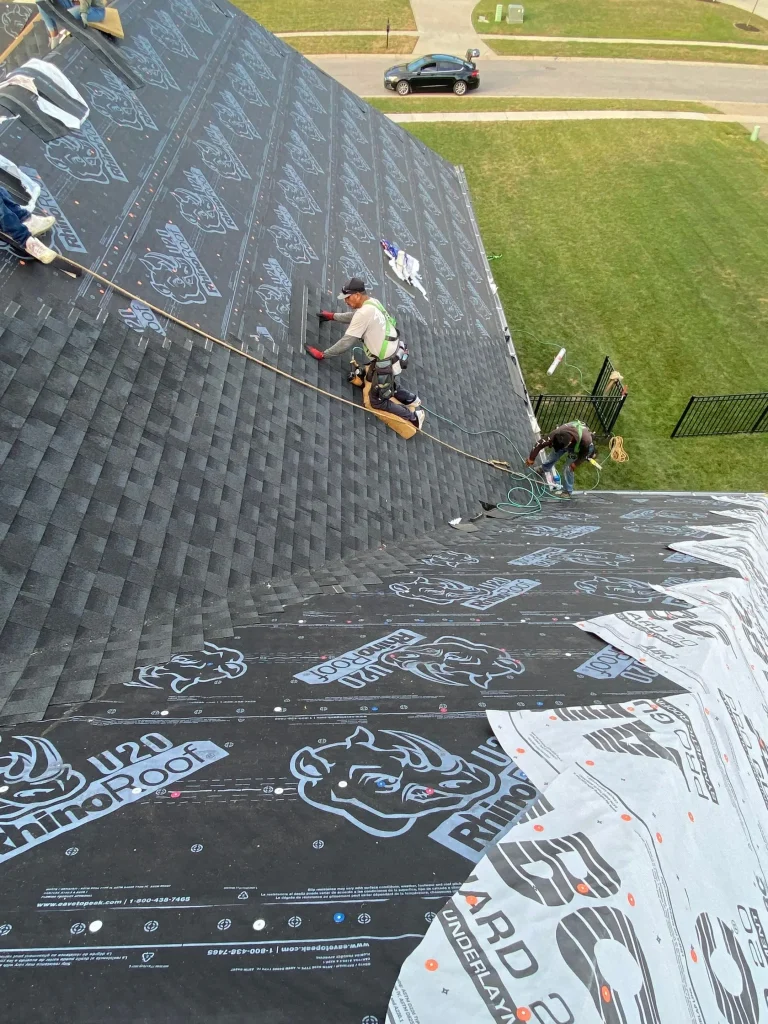 Roofing crew in safety harnesses installing architectural shingles over RhinoRoof U20 synthetic underlayment at a roof valley on a Louisville, KY home by AIC Roofing & Construction.