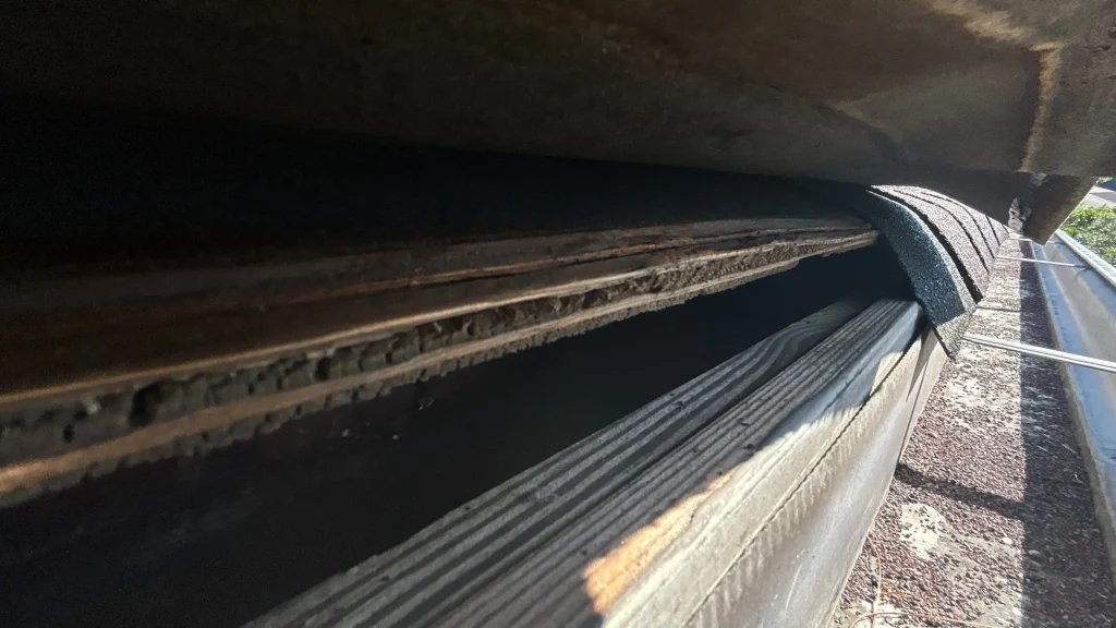 Louisville KY Eave & Gutter Inspection | AIC Roofing & Construction Close-up of rotted roof eave with delaminated decking above a debris-filled gutter on a Louisville, KY home, documented for repair by AIC Roofing & Construction.