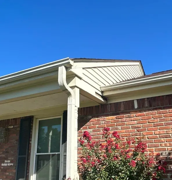 Close view of seamless white K-style gutters and a downspout at a roof corner on a Louisville, KY brick home, installed by AIC Roofing & Construction.