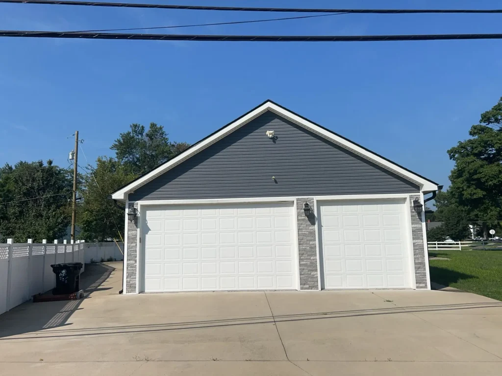 Front view of a Louisville, KY home with new gray siding, white trim, and stone accents around a double garage, installed by AIC Roofing & Construction.