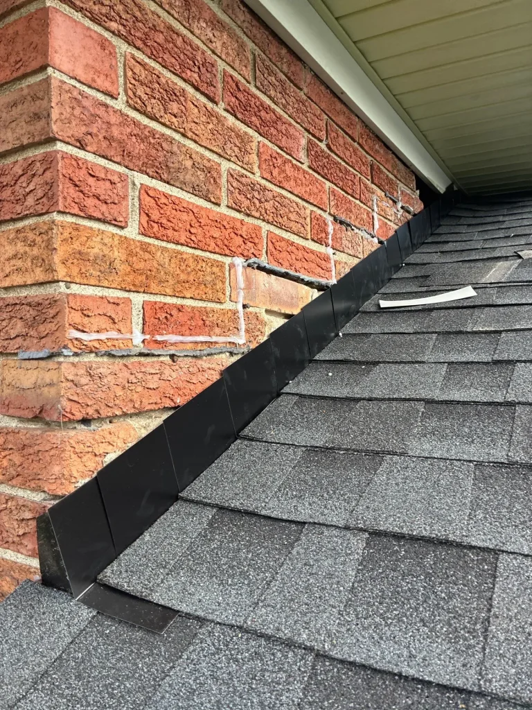 Louisville KY Step Flashing Installation | AIC Roofing & Construction Close-up of new black metal step flashing along a brick sidewall where an asphalt shingle roof meets the wall, installed by AIC Roofing & Construction in Louisville, KY.