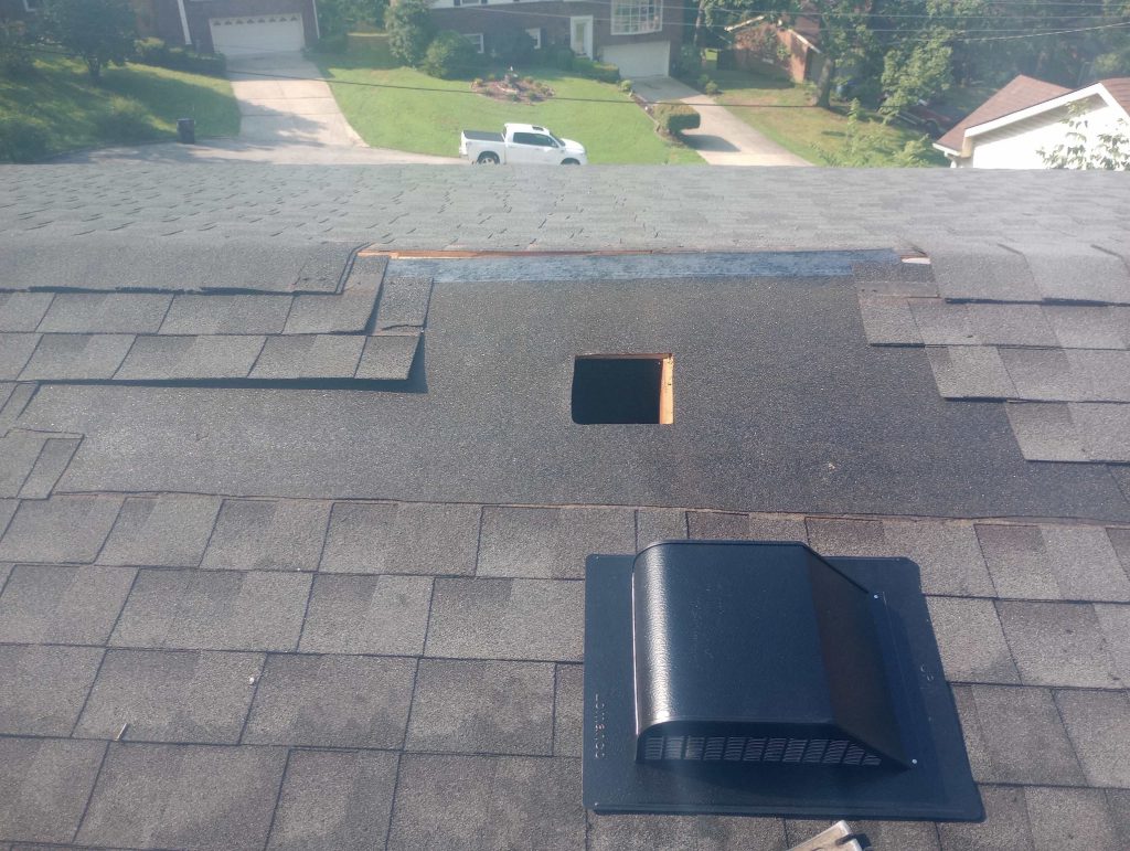 Missing Shingles – Louisville KY Roof Inspection | AIC Roofing & Construction Louisville, KY asphalt shingle roof with missing shingles near the ridge, exposing underlayment and a square deck cutout; box vent visible in foreground.
