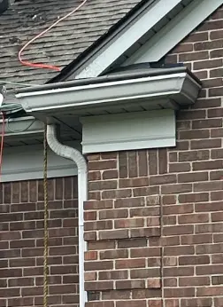 Newly installed white aluminum gutter and downspout on a brick Louisville home at the roof corner