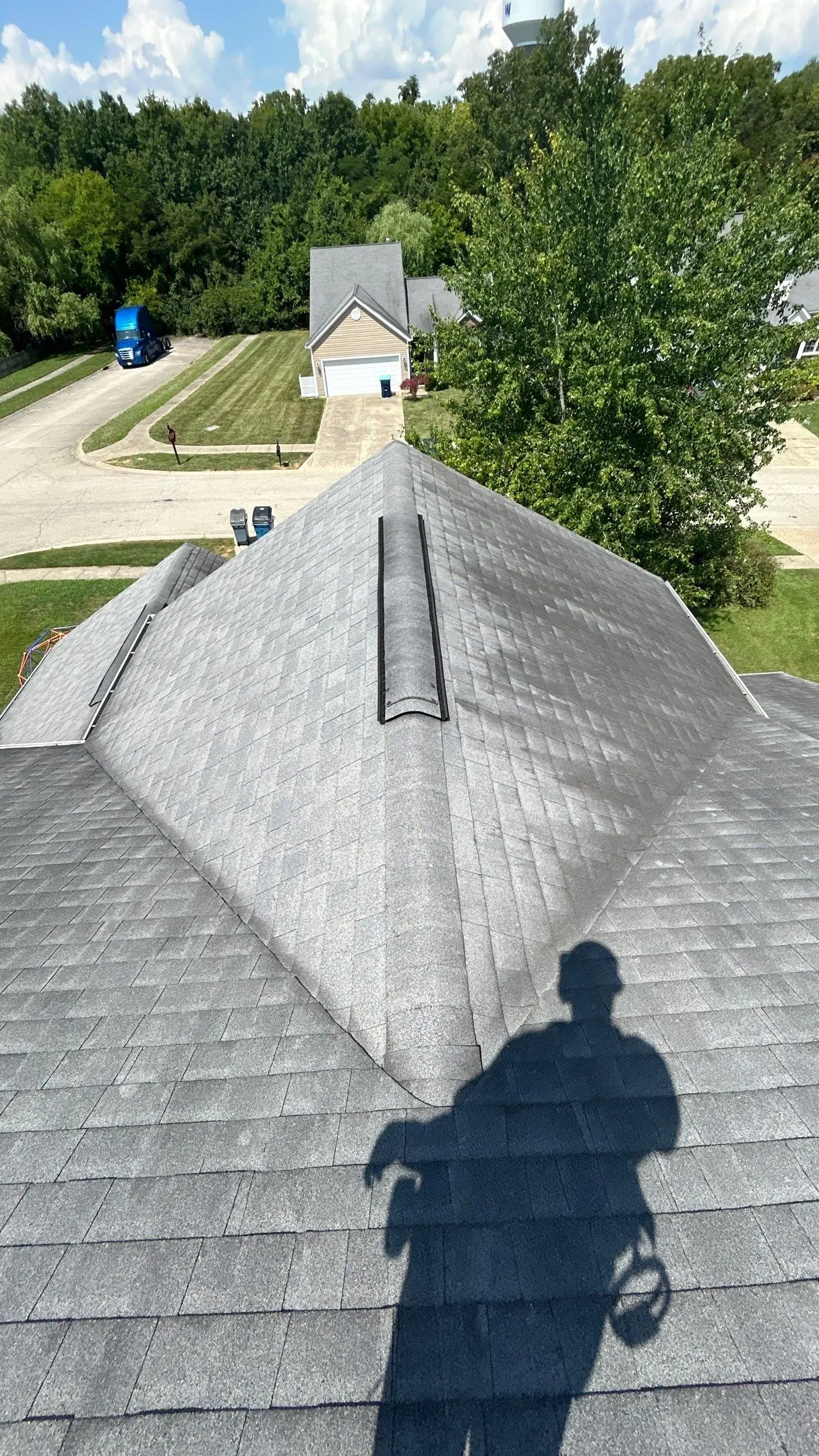 Shingle Discoloration – Louisville KY Roof Inspection | AIC Roofing & Construction Gray asphalt shingle roof with continuous ridge vent and light/dark discoloration patterns; inspector’s shadow visible on a Louisville home.