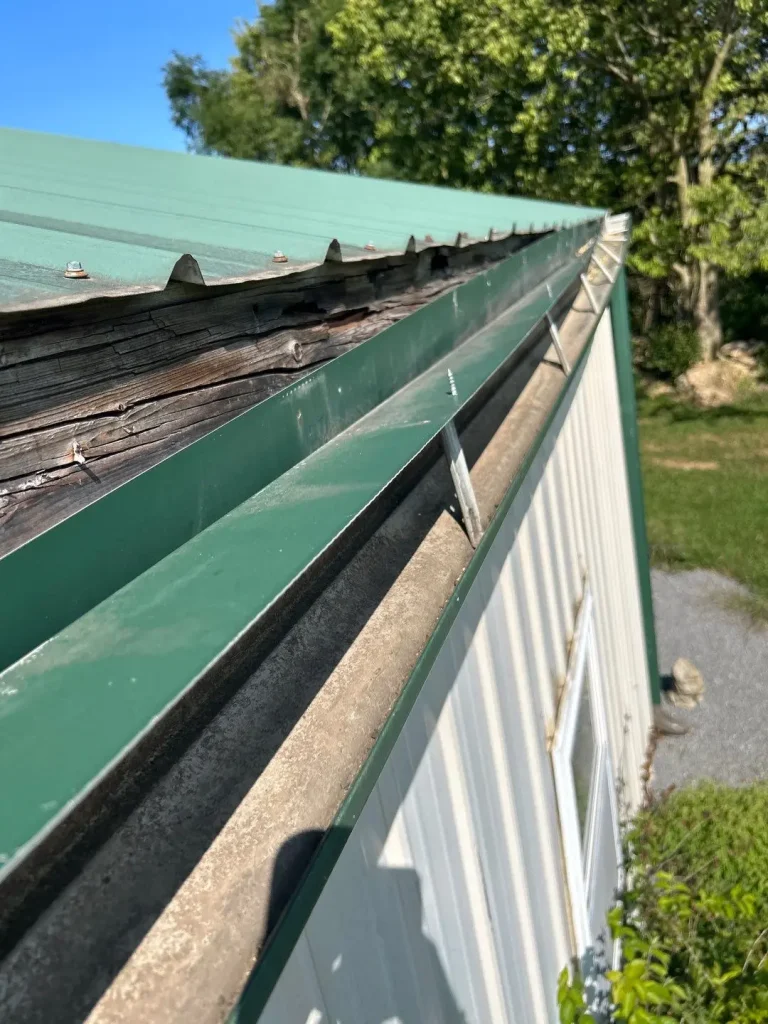 Damaged fascia board and gutter system on a metal roof building, showing signs of rot and deterioration.