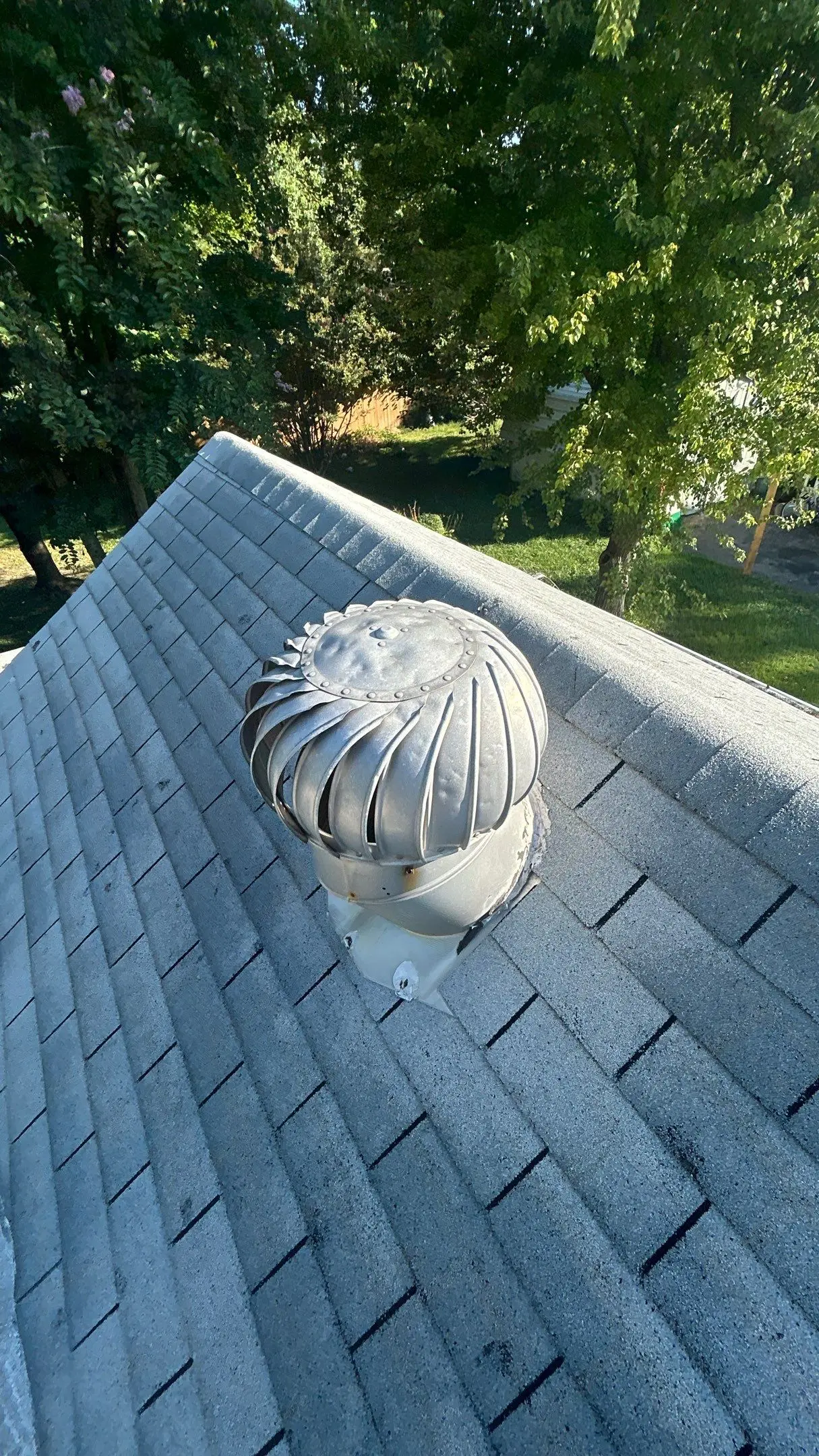 Roof turbine vent with hail damage dents on top of faded gray asphalt shingles.