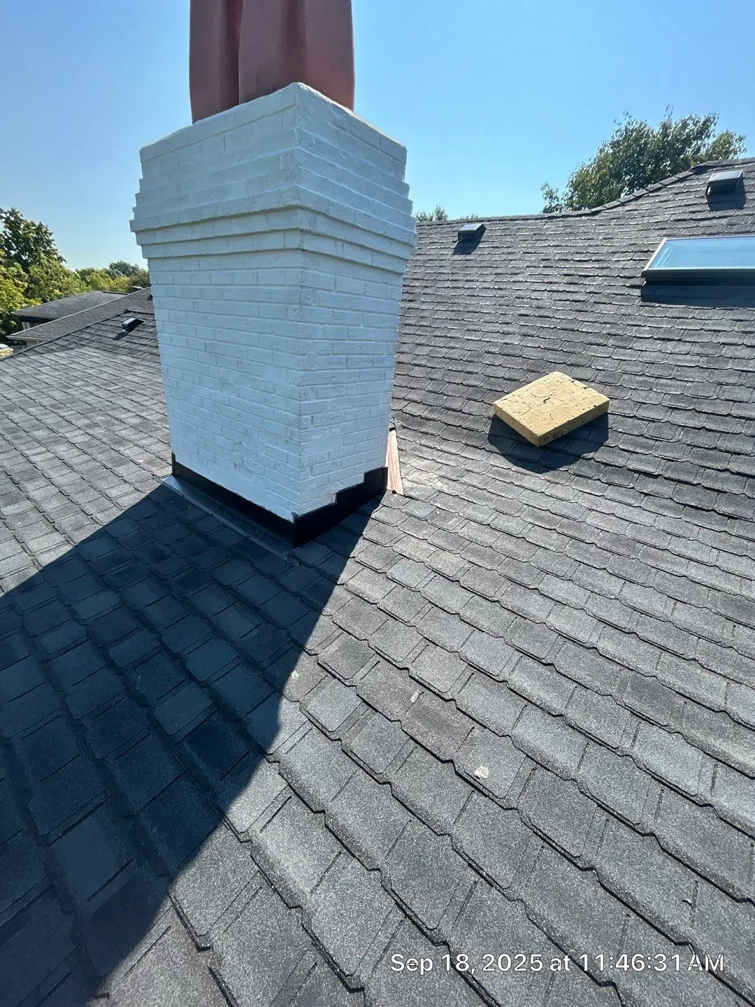 Chimney Flashing Inspection on Louisville Roof Louisville roof with a white brick chimney, black flashing, asphalt shingles, and a skylight visible in the background.