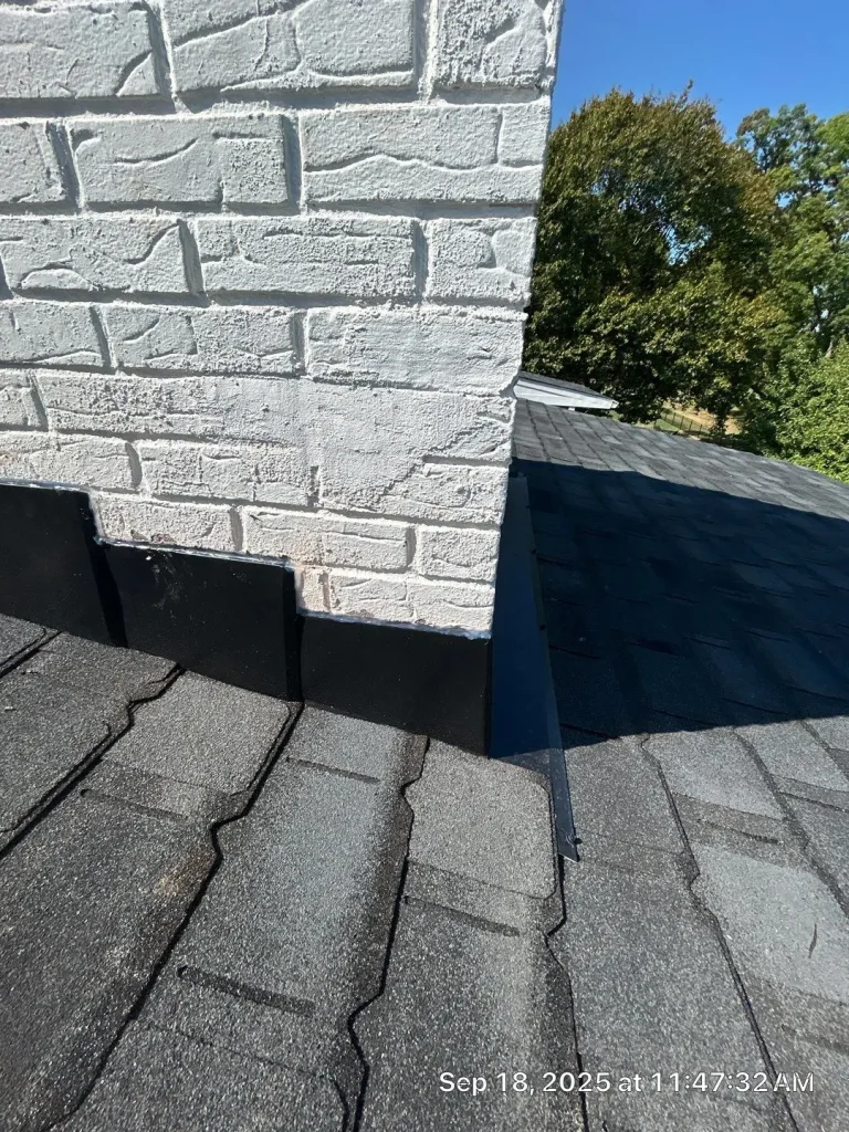 Close-up of a white brick chimney with black roof flashing on a shingle roof in Louisville, showing proper installation around the base.
