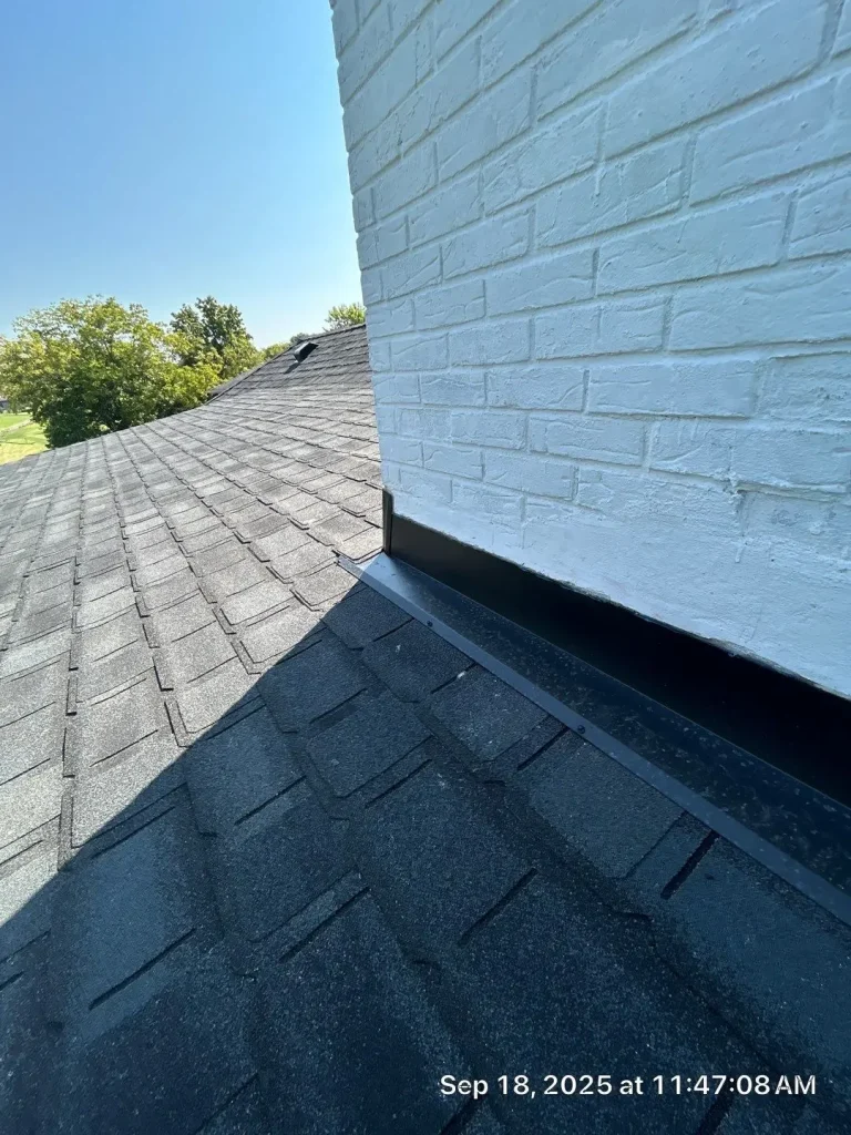 Close-up of white brick chimney with new black flashing installed on a Louisville roof with asphalt shingles.