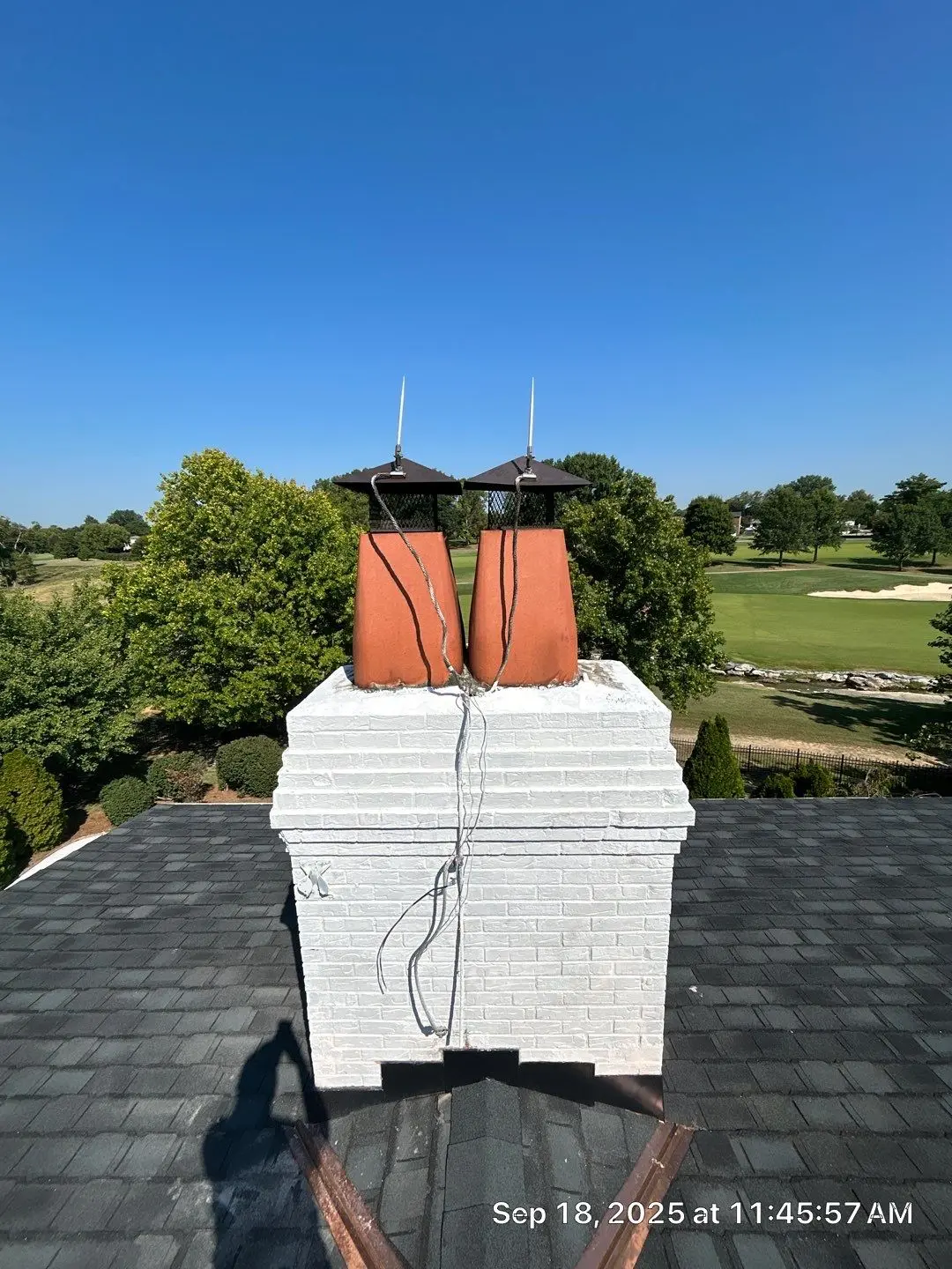 Chimney Flashing Inspection on Louisville Roof Louisville home chimney with white brick base, dual chimney caps, and lightning protection wires on a shingle roof.