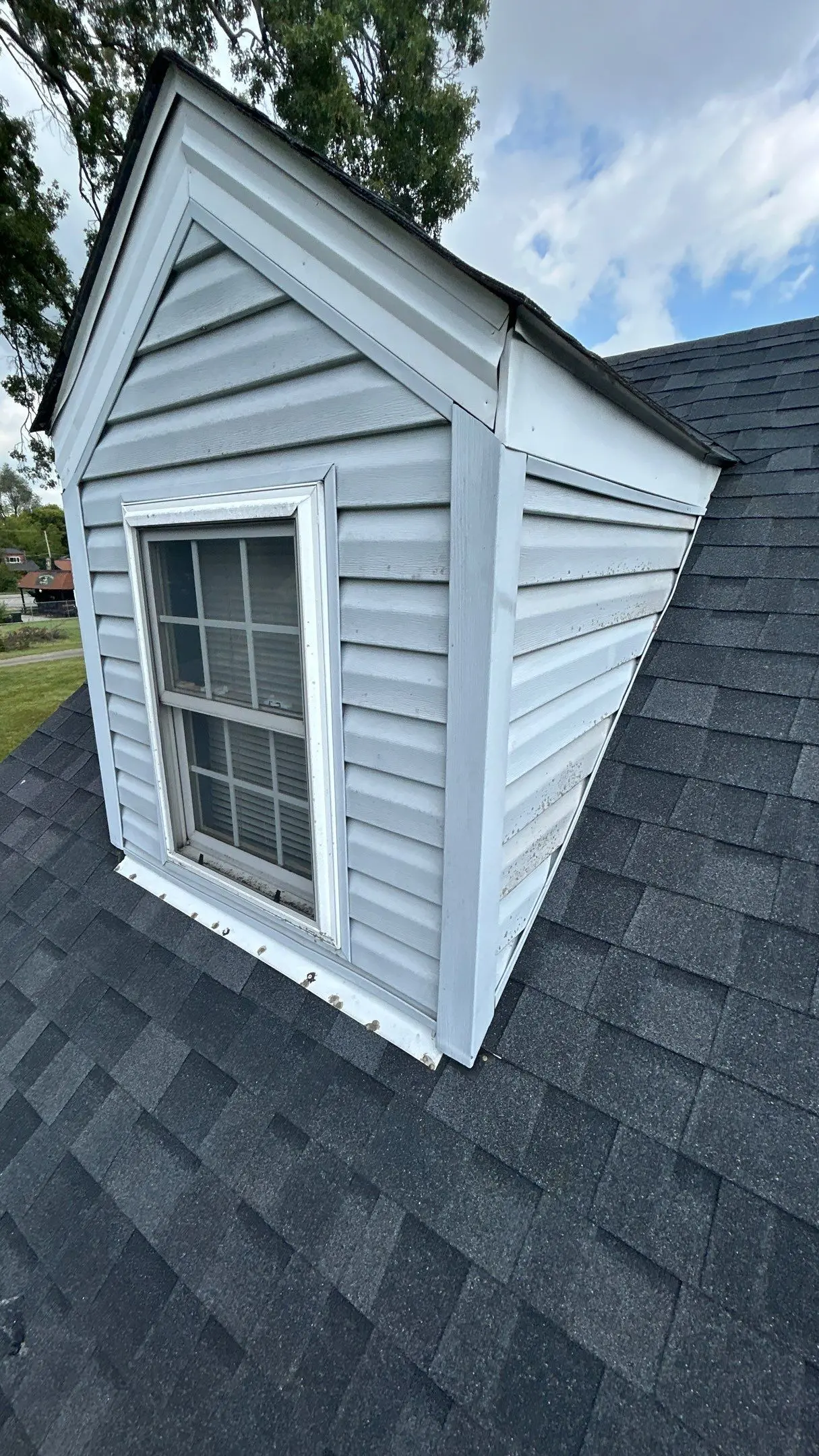 Louisville home dormer with gray vinyl siding and asphalt shingles, showing siding stains and flashing around the window base.