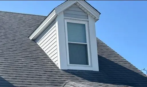 Dormer window on a Louisville home with gray vinyl siding and dark asphalt shingles under a clear blue sky.