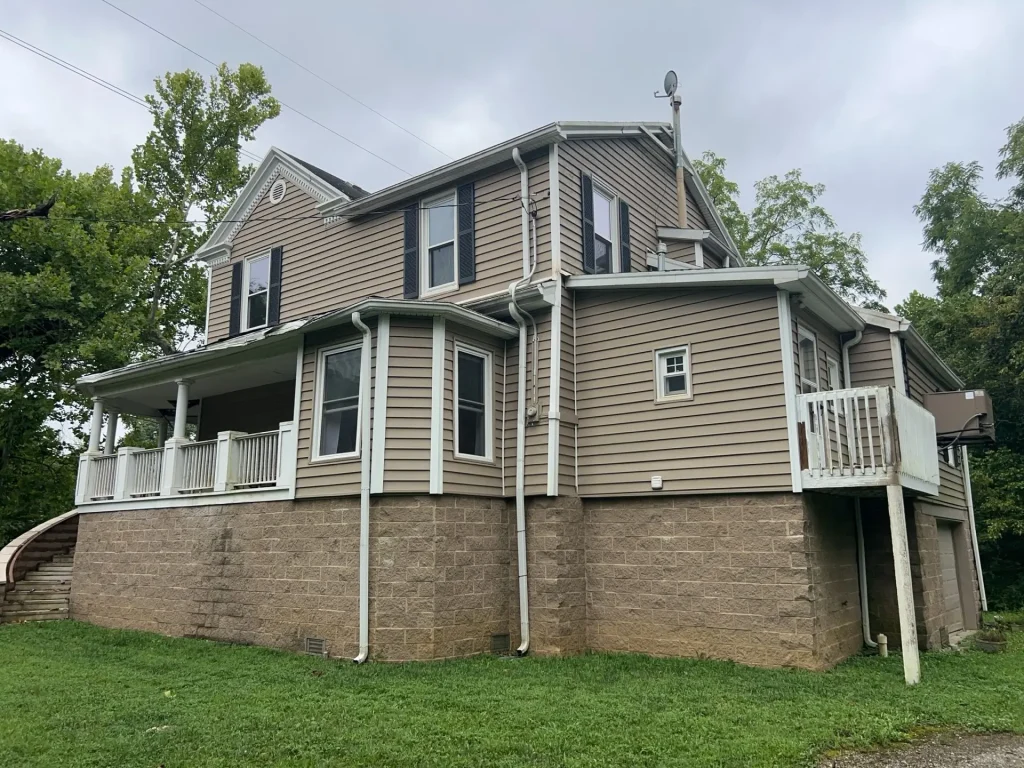 Two-story tan house in Louisville with vinyl siding and white trim, showing areas that may require siding repair and maintenance.