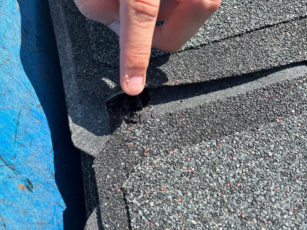 Shingle Repair in Progress on Louisville Roof Close-up of a hand lifting a damaged asphalt shingle on a Louisville roof, showing wear and repair needs.