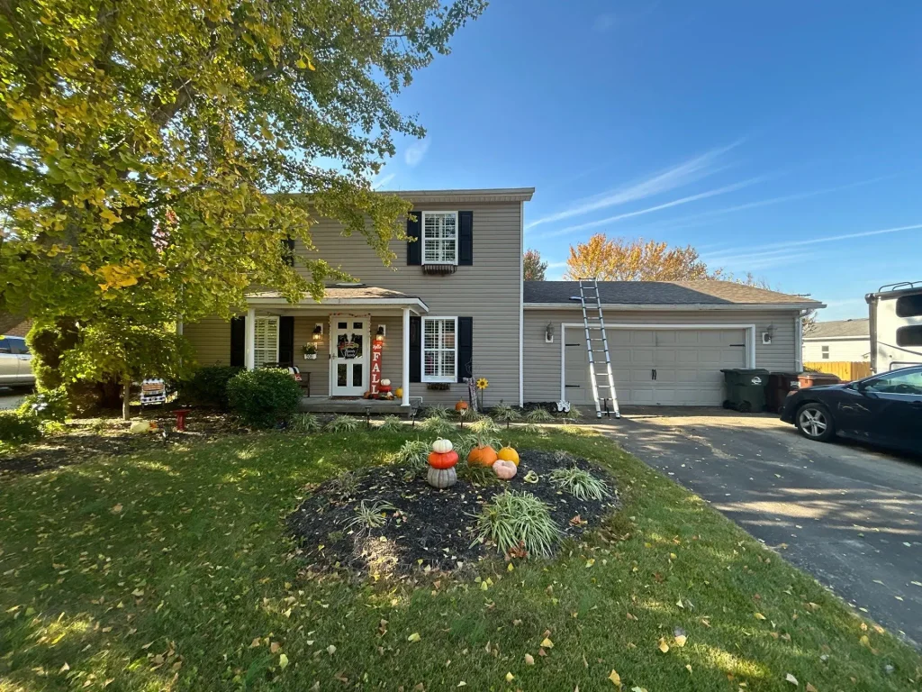 Front view of a Louisville home with tan vinyl siding and white trim, showing a ladder against the garage for siding repair work.