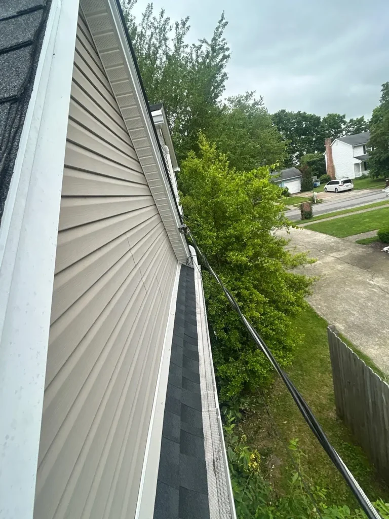 Louisville home with tan vinyl siding and black roof shingles, showing warped and uneven siding panels needing repair.