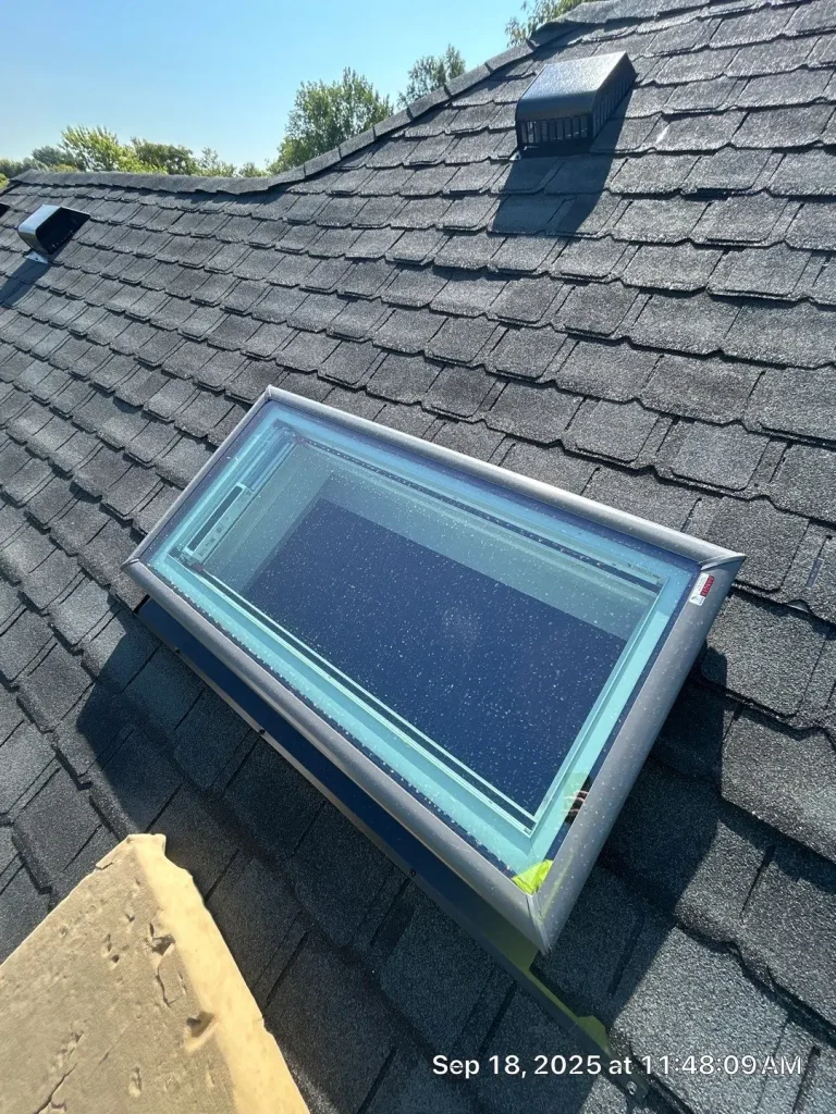 Louisville roof with a skylight window installed among dark asphalt shingles and roof vents under clear blue sky.