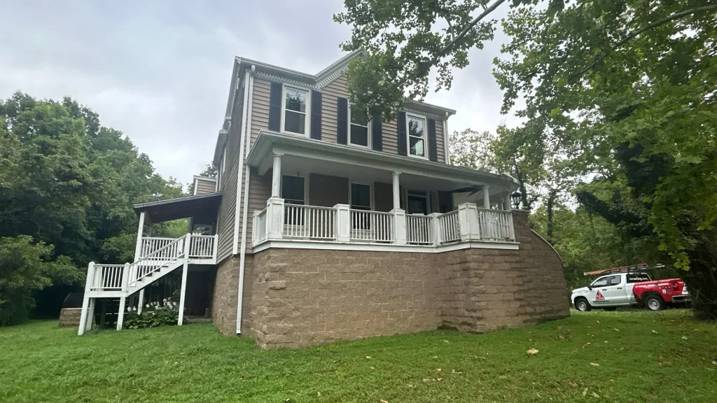 Front view of a two-story Louisville home with tan vinyl siding, white porch railings, and a contractor’s truck parked nearby for siding repair.
