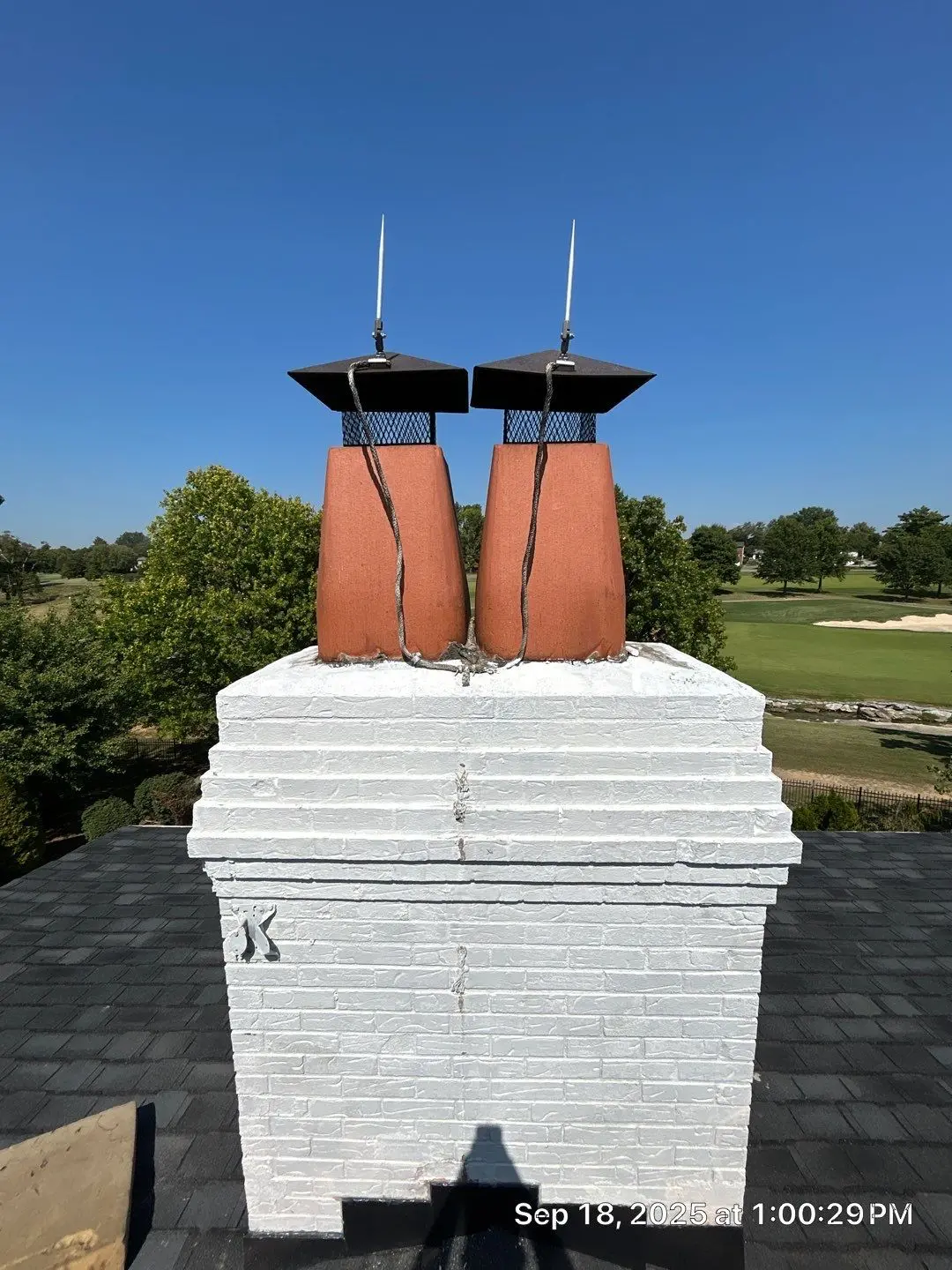 Chimney Flashing Inspection on Louisville Roof Louisville roof chimney with white brick base, dual red clay stacks, and metal chimney caps with lightning rods.