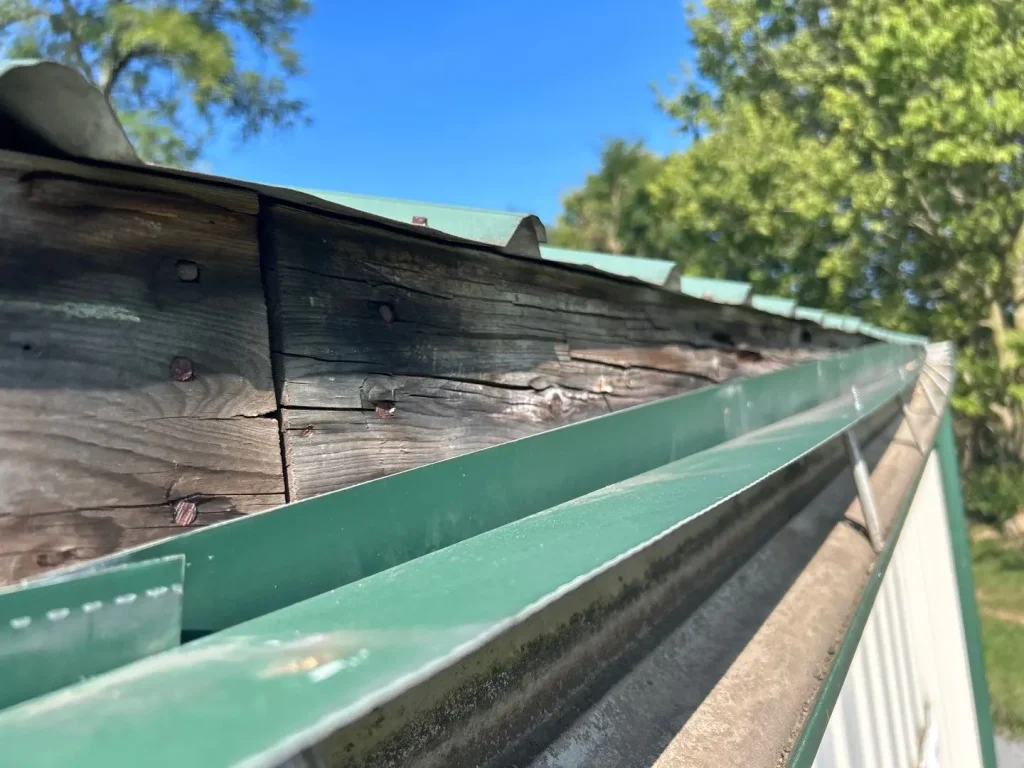 Rotted fascia board and damaged gutter system on a metal roof building.
