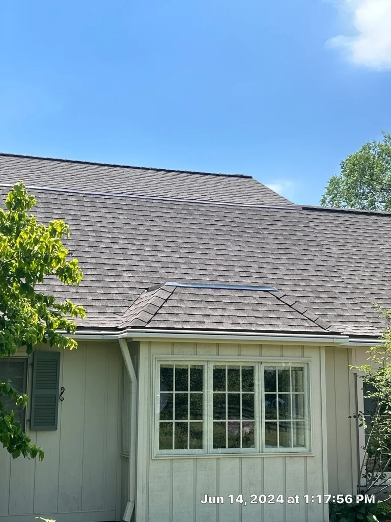 Close-up of a Simpsonville home after a roof replacement with new asphalt shingles and a skylight under a clear blue sky.