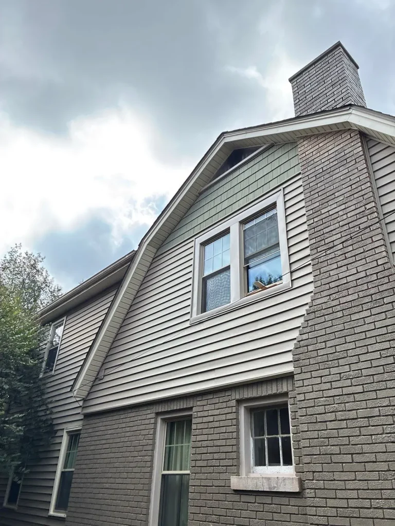 Two-story Louisville home featuring a mix of light gray brick and beige vinyl siding with green shake accents near the gable and chimney.