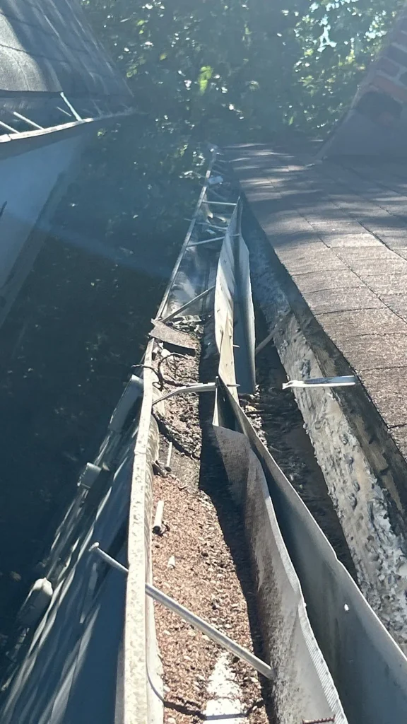 Broken Gutter with Debris on Louisville Home Close-up of a damaged gutter pulling away from the roofline of a Louisville home, showing debris buildup and sagging metal panels.