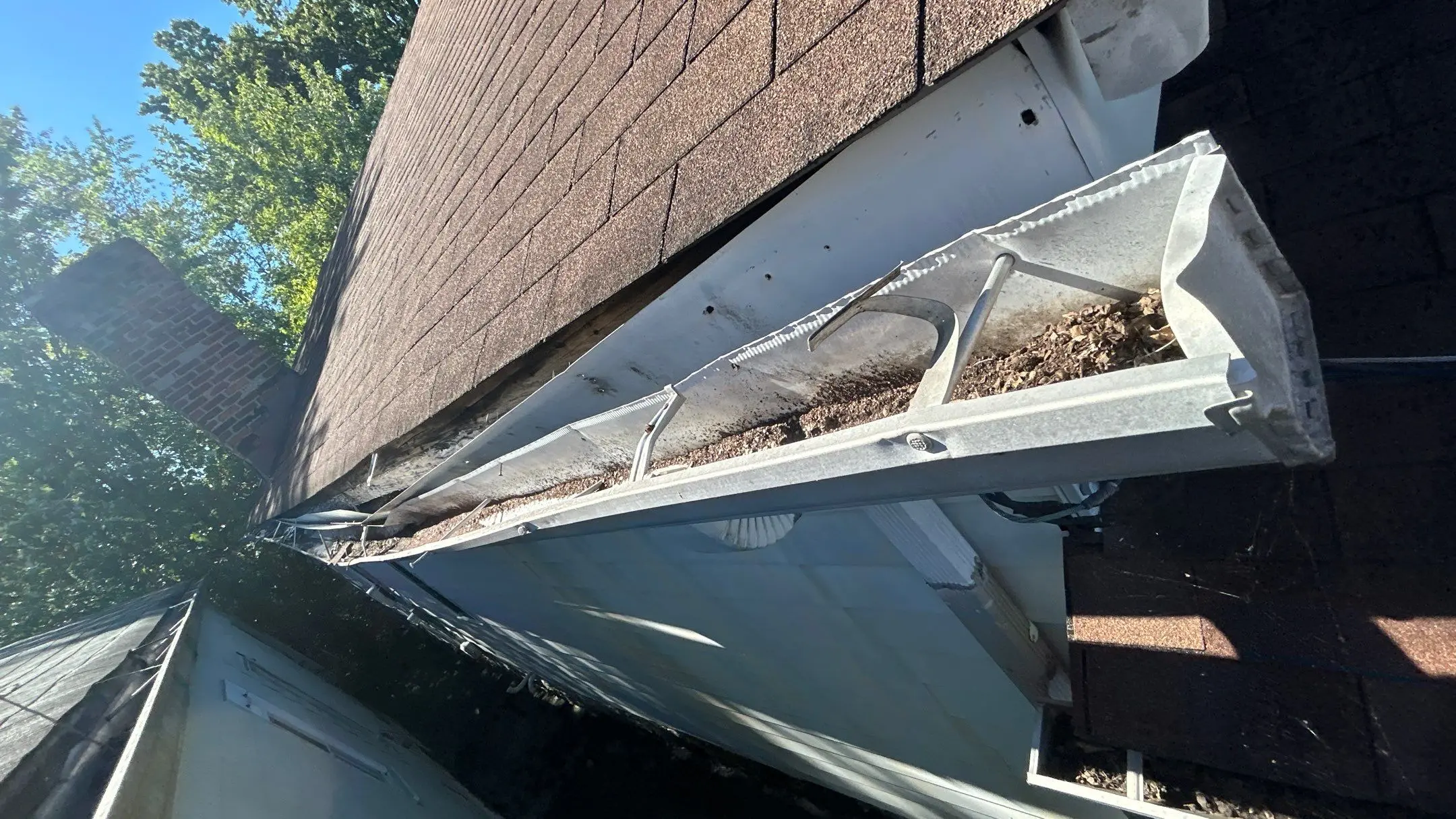 Old Gutter with Water Damage on Louisville Home Detached and clogged gutter pulling away from a roofline on a Louisville home, showing debris buildup and signs of water damage under the shingles.