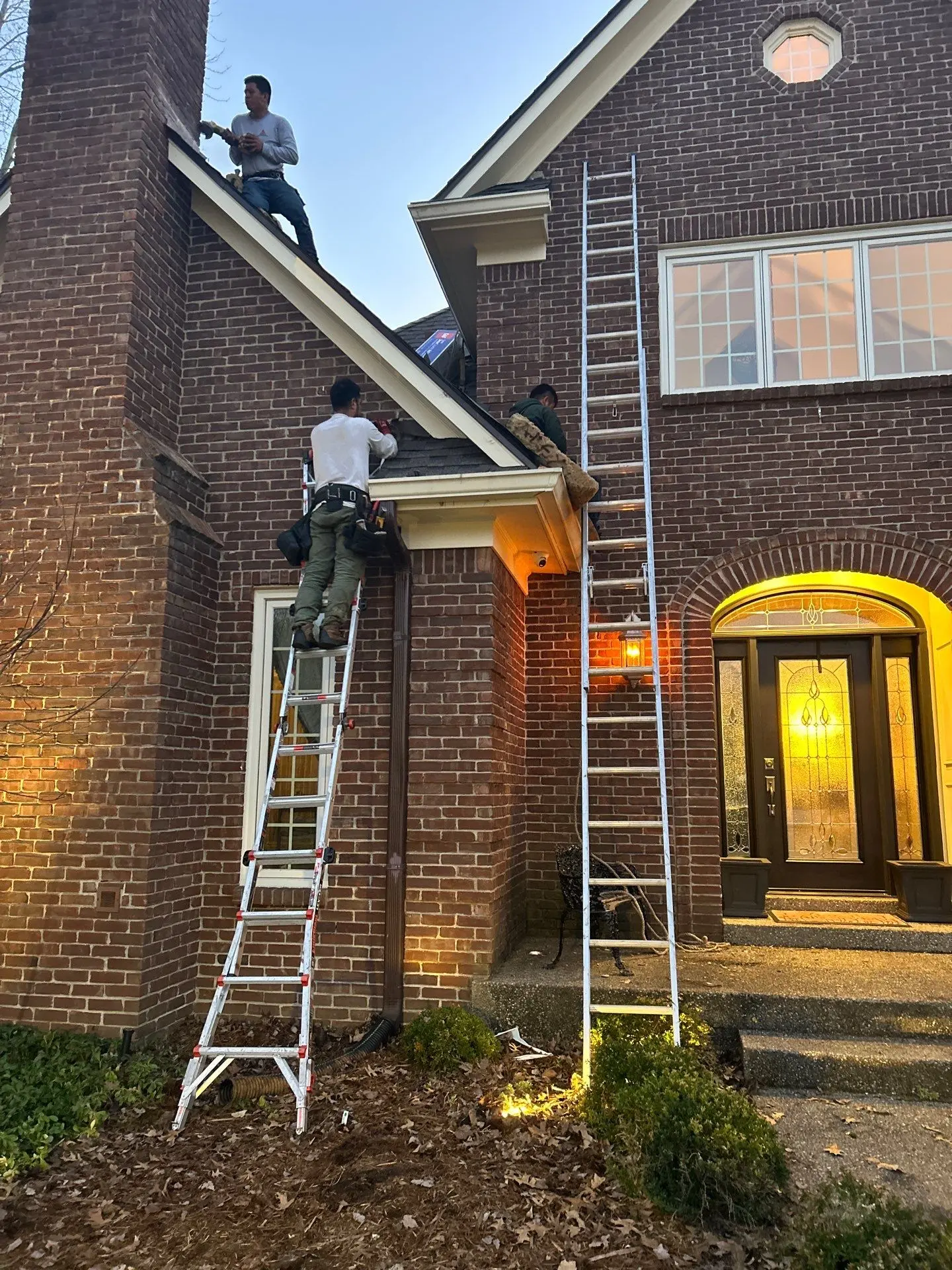 Roofing crew repairing shingles and flashing on a two-story brick home in Louisville, Kentucky, using ladders and safety gear near the front entryway.