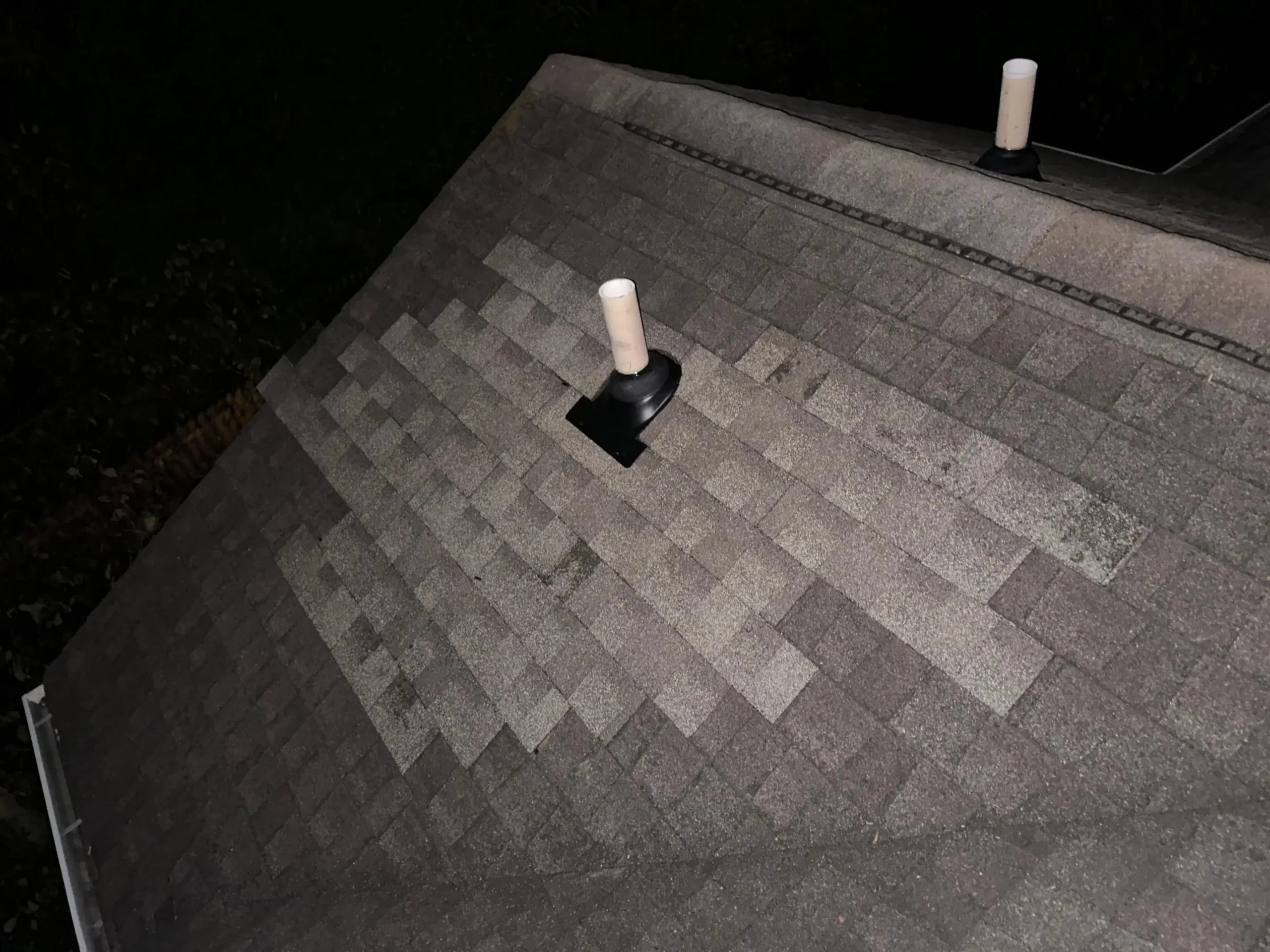 Repaired roof section on a Louisville home showing new shingles installed around plumbing vent pipes at night.