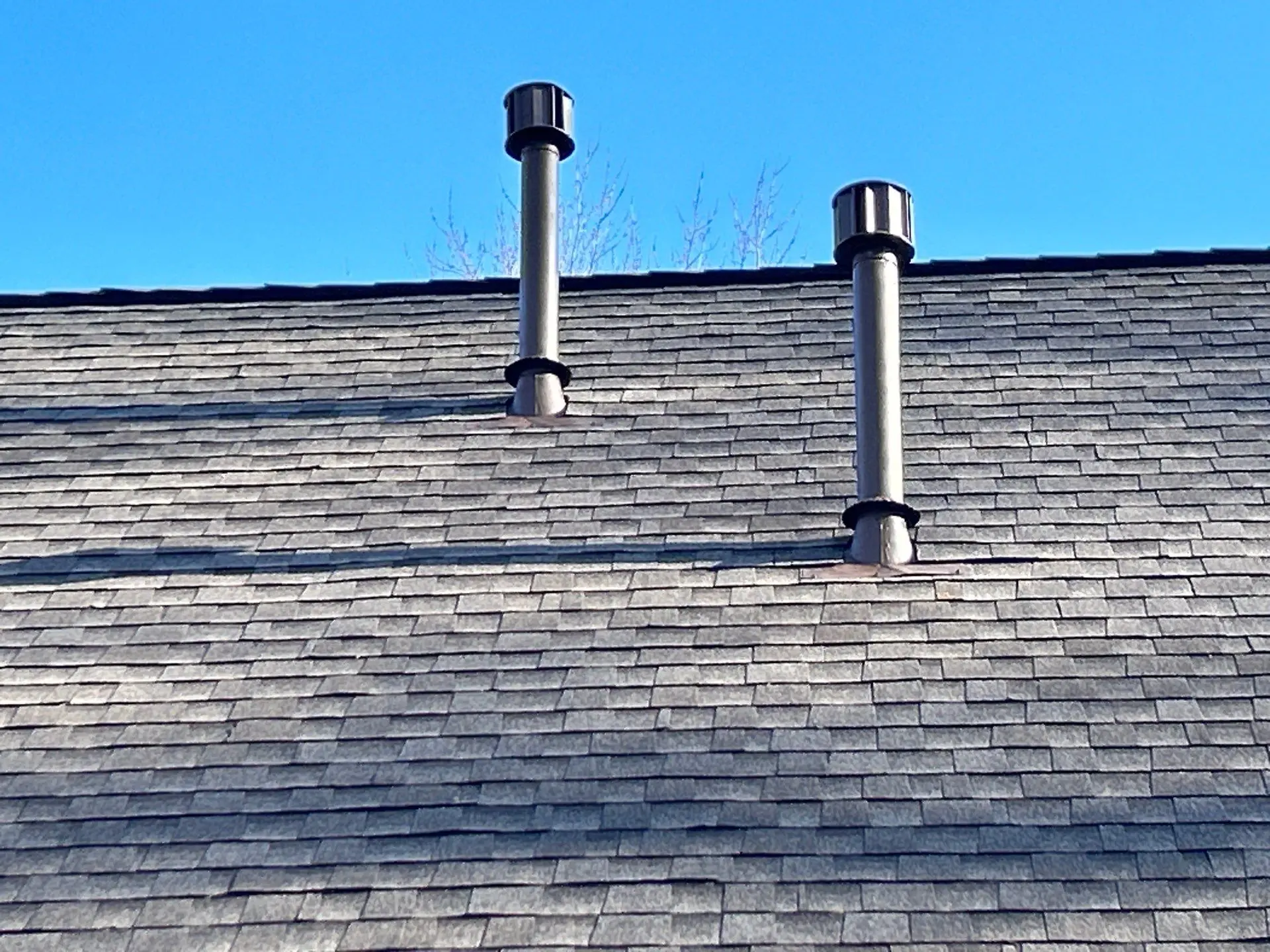 Two metal roof vent pipes installed on an asphalt shingle roof under a clear blue sky in Bardstown, Kentucky.