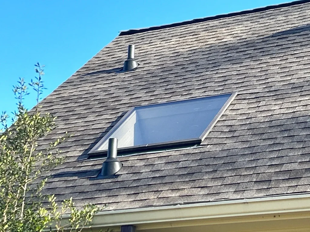 Asphalt shingle roof with skylight and vent pipes on a Louisville, Kentucky home under a clear blue sky.