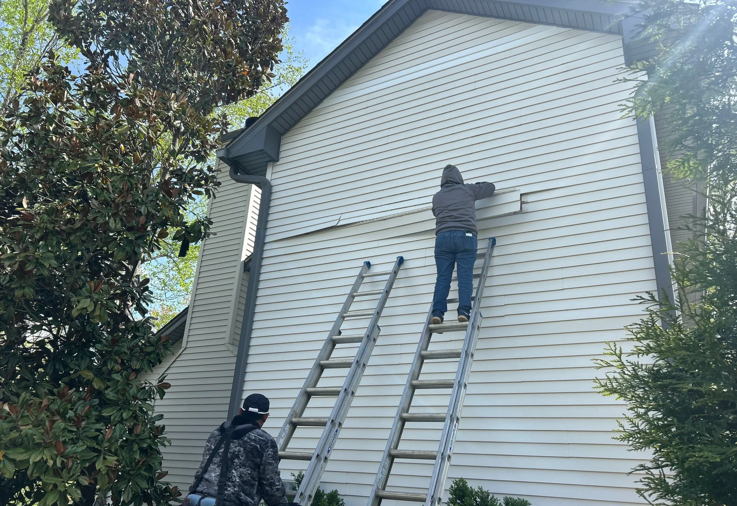 Contractors repairing vinyl siding on a Shelbyville, Kentucky home using ladders and professional tools.