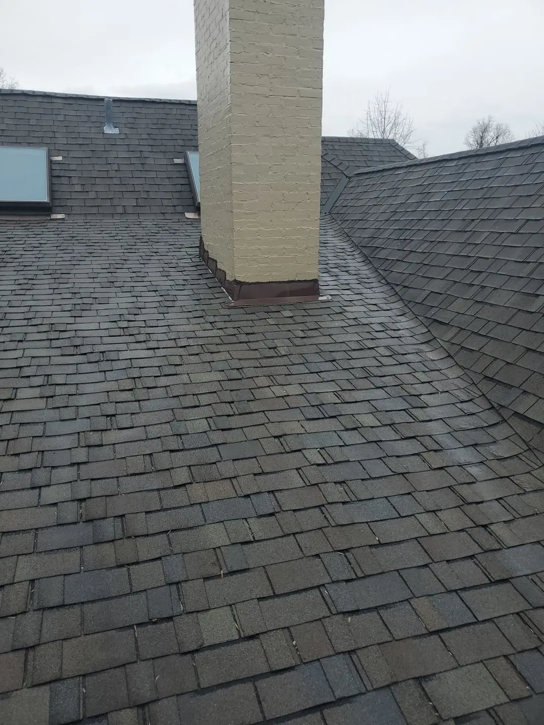 Chimney on a shingle roof with deteriorating flashing and visible signs of needed repair.
