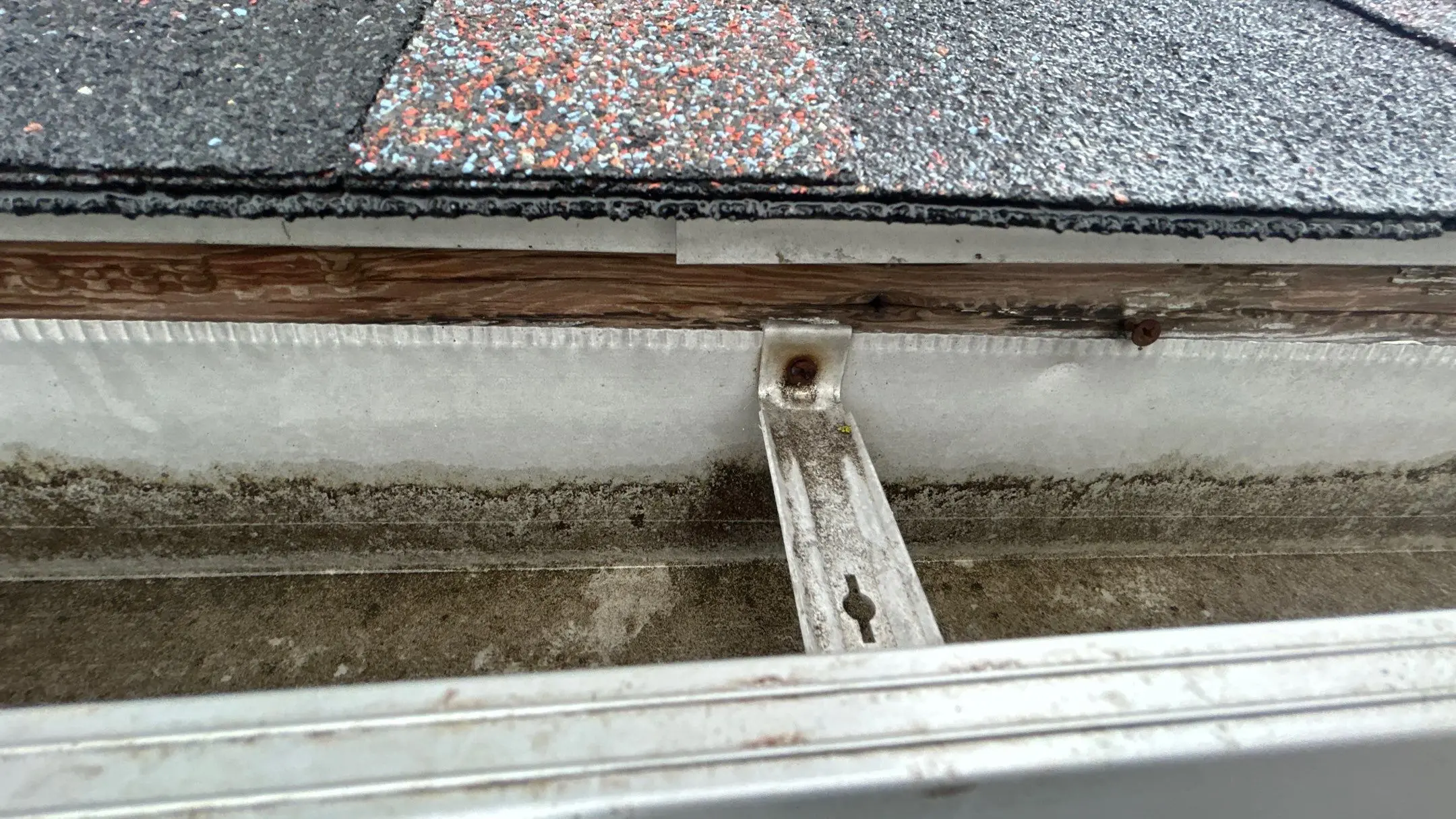 Old Gutter with Water Damage on Louisville Home Close-up of rotting fascia board, dirty gutters, and rusted brackets beneath asphalt shingles on a Kentucky home.