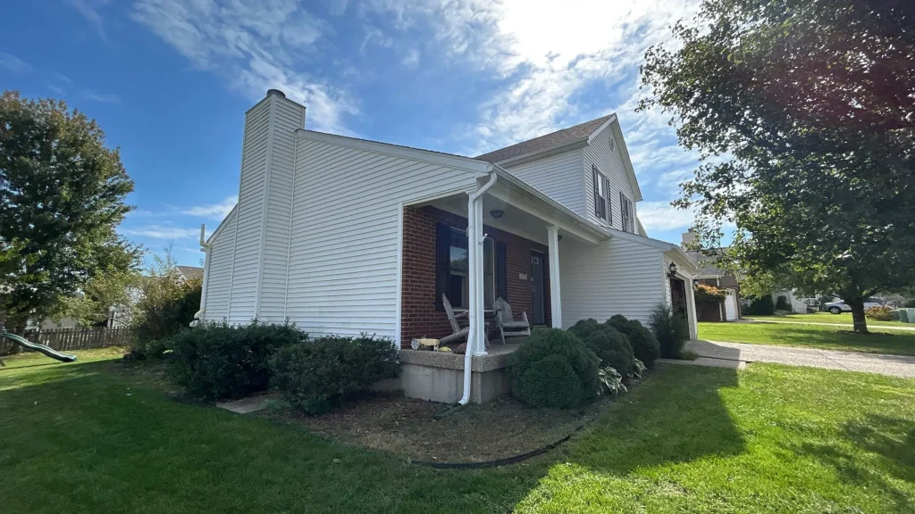 Front corner view of a Louisville KY home with white vinyl siding, brick accent entryway, and a covered porch on a sunny day.