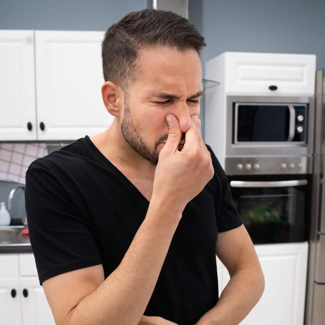 Man in a kitchen holding his nose due to a strong musty smell caused by moisture or a roof leak in his Middletown KY home.