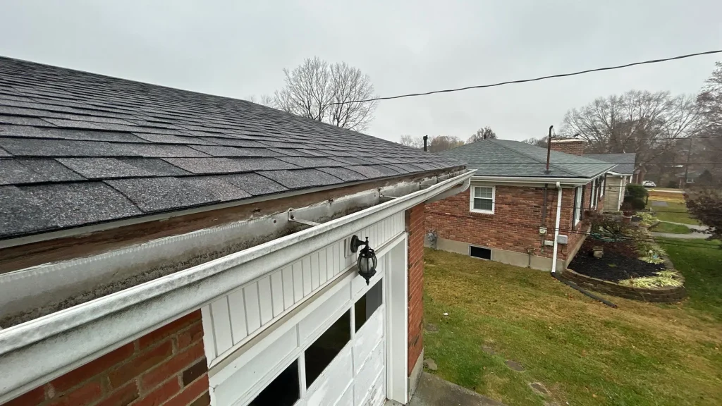 Broken Gutter with Debris on Louisville Home Sagging metal gutters with fascia rot and grime buildup along the garage roofline of a Louisville KY home.