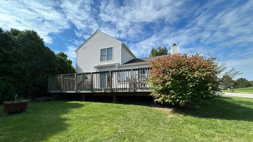Back view of a Louisville KY home with white vinyl siding, a raised wooden deck, and manicured lawn under a bright blue sky.