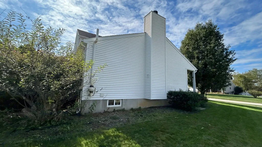 Side view of a Louisville KY home with clean white vinyl siding, a tall chimney, and well-kept landscaping under a blue sky.