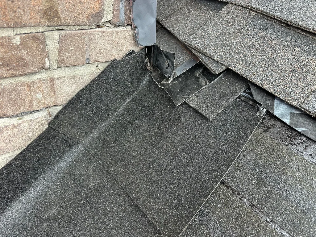 Damaged asphalt shingles near chimney flashing on a Louisville, KY home